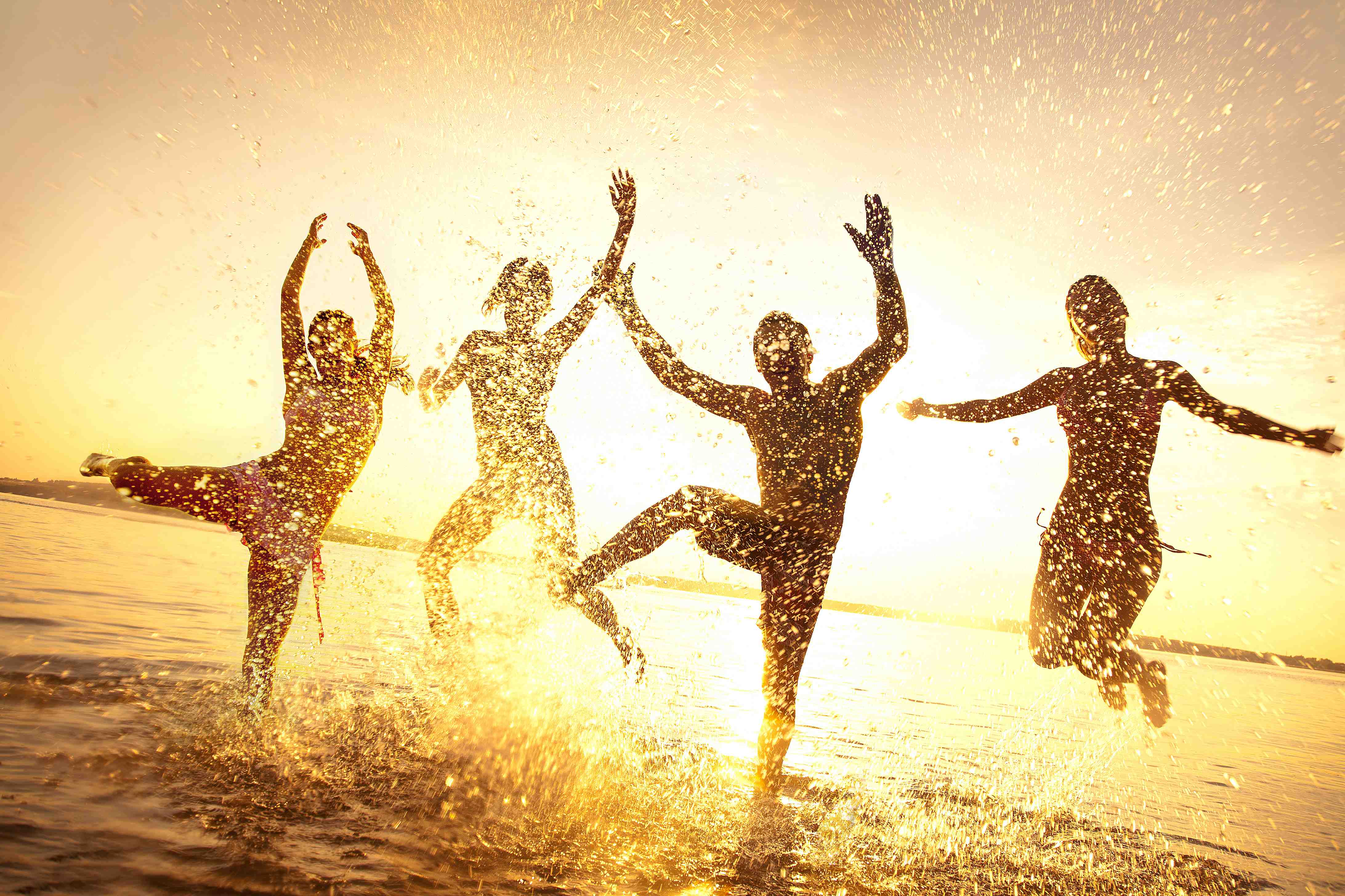 Eine Gruppe Menschen tanzt ausgelassen gemeinsam im flachen Wasser vor der untergehenden Sonne