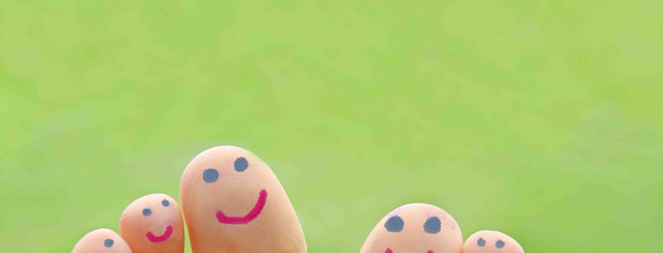 Zehen mit aufgemalten lachenden Gesichtern und Gänseblümchen vor grünem Hintergrund